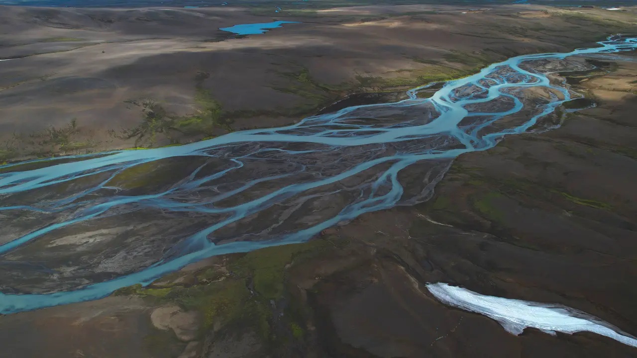Aerial view of turquoise glacial river channels crossing dark Icelandic terrain