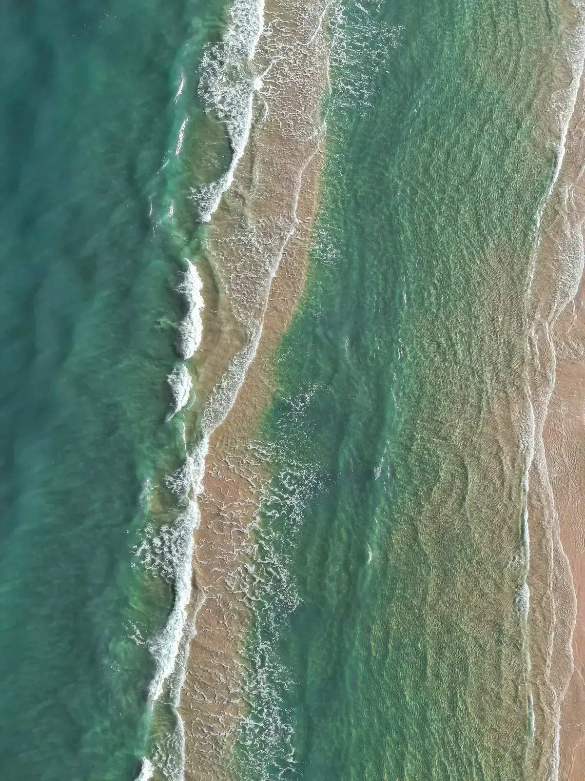 Aerial view of muted teal waves meeting the shoreline